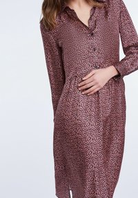 Robe à manches longues en tissu rose foncé avec un motif floral, dotée d'une patte de boutonnage à l'avant et d'une taille froncée.
