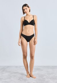 Zwarte draadloze beha met een diepe halslijn en dunne bandjes, gecombineerd met bijpassende zwarte hipster slip met kanten rand.