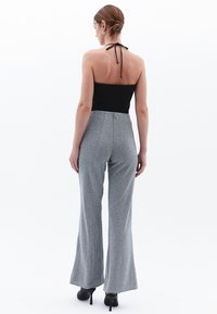 Zwarte halter bodysuit gecombineerd met zilveren uitlopende broeken, met een gestructureerde afwerking en subtiel patroon, gedragen met zwarte hoge hakken.