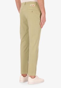 Pantaloni in cotone verde chiaro con una vestibilità slim, dotati di una tasca posteriore e di una piccola etichetta del marchio. Abbinati a sneaker bianche.