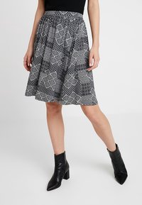 Svartvit mönstrad kjol med utsvängd design och elastisk midja, parat med svarta ankelskor med tjock klack.