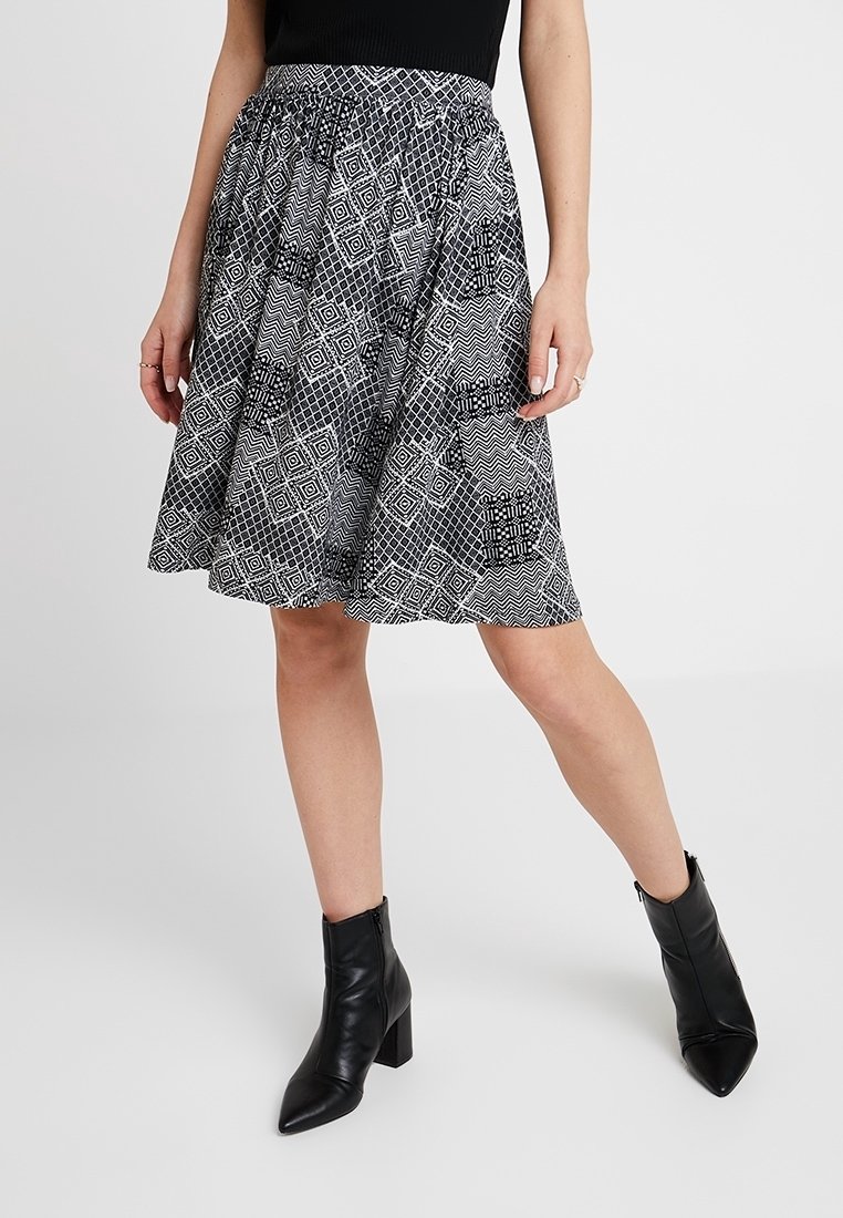 Svartvit mönstrad kjol med utsvängd design och elastisk midja, parat med svarta ankelskor med tjock klack.