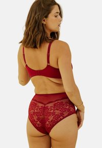 Ensemble de soutien-gorge rouge et culotte taille haute. Le soutien-gorge dispose d'un tissu lisse avec des bretelles réglables ; la culotte présente des détails en dentelle avec des motifs floraux.