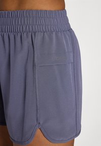 Athletic shorts in a soft, stretchy gray fabric with an elastic waistband, side pocket, and curved hemline for ease of movement.
