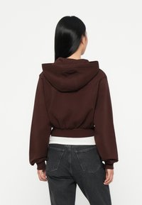 Brown cropped hoodie with a hood, ribbed hem, and balloon sleeves, paired with dark jeans. Simple design, cotton-like texture.