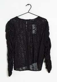 Top in pizzo nero appeso a un gancio, con un motivo floreale a rilievo, maniche arricciate e scollo rotondo.