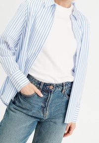 Blauw-wit gestreepte button-up shirt met een ontspannen pasvorm, gecombineerd met lichtblauwe denim jeans met een rits- en knoopsluiting.