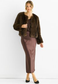 Woman wearing a dark brown faux fur jacket over a sequined top, paired with a satin midi skirt and black high-heeled shoes.