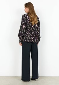 Långärmad, löst sittande blus i mörklila med ett vågigt beige mönster, parat med högmidjade svartabyxor och stilettklackar.