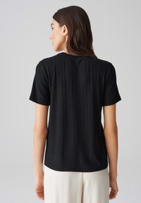 Zwart geribbeld T-shirt met korte mouwen en een rechte zoom, met een subtiele textuur. Het heeft een ronde halslijn en is gemaakt van zachte, lichte stof.
