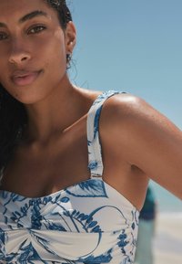Weiß-blauer Badeanzug mit floralem Muster und gerafftem Design. Verfügt über verstellbare Träger und metallische Hardware-Akzente.