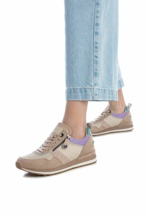 Zapatillas beige que presentan una mezcla de materiales, incluyendo ante y malla, con un detalle de cremallera, acentos morados y una suela texturizada.