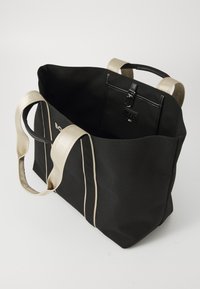 Borsa tote nera con manici beige chiaro. Caratterizzata da un'apertura superiore, cuciture laterali a contrasto e una tasca interna con clip.