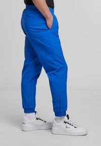Blue lightweight jogger pants with elastic waistband and cuffs, featuring side pockets. Paired with white sneakers and blue-striped socks.