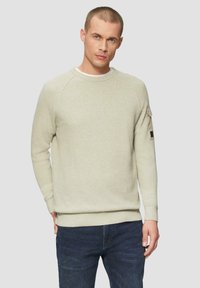 Jasno beżowy sweter z dzianiny o okrągłym dekolcie i raglanowymi rękawami. Ma teksturowaną tkaninę oraz małą kieszonkę na rękawie.