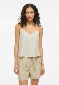 Top senza maniche grigio chiaro con scollatura a V, realizzato in tessuto traspirante, abbinato a pantaloni corti beige a vita alta con cintura annodata.