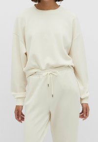 Lichtbeige sweatshirt met een relaxte pasvorm, ronde hals en een ontwerp met verlaagde schouders. Gecombineerd met bijpassende joggers met een trekkoord in de taille.