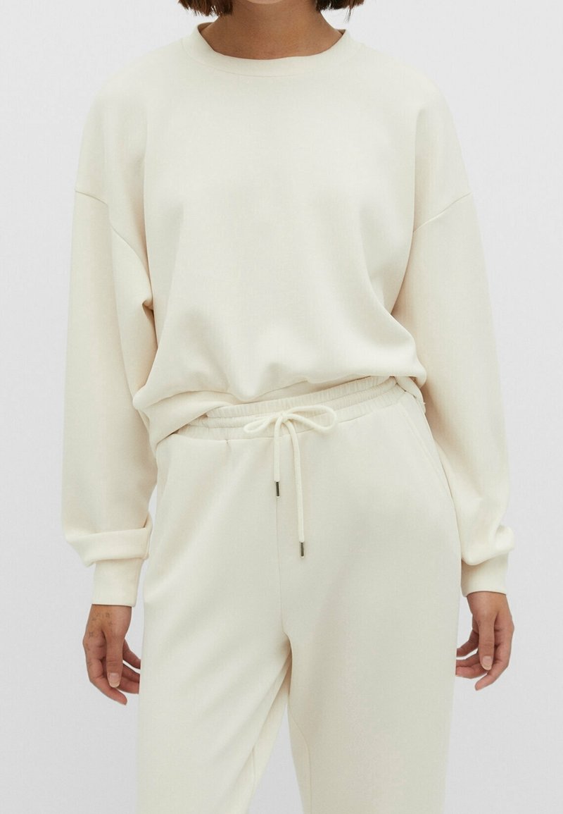Lichtbeige sweatshirt met een relaxte pasvorm, ronde hals en een ontwerp met verlaagde schouders. Gecombineerd met bijpassende joggers met een trekkoord in de taille.