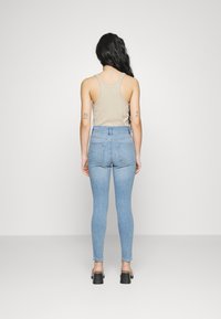 Ljusblå högmidjade jeans med en figurnära design och lätt stretch. Matchas med en beige tanktop, vilket ger en enkel och avslappnad look.