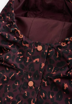 Närbild på en vinröd jacka med svart och orange leopardmönster, utrustad med oranga tryckknappar och justerbara dragsnören på huvan.