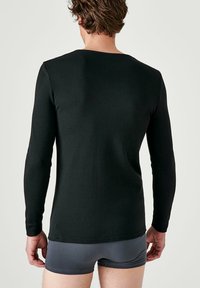 Zwarte langemouwen shirt van zachte stof, aansluitend design, met een ronde halslijn en zonder zichtbare logo's, gecombineerd met grijze shorts.