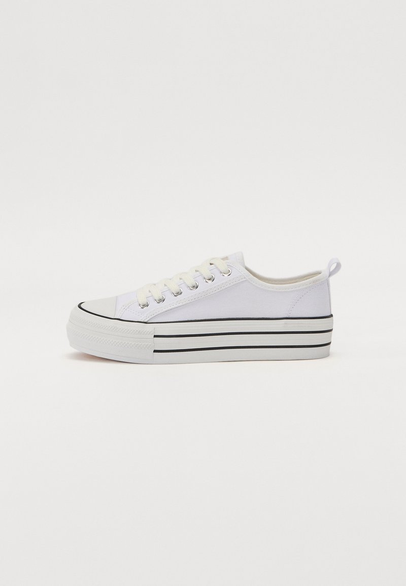 Sneaker bianca in tela con punta arrotondata, suola nera e dettagli a strisce orizzontali nere. Include lacci e un anello sul tallone per una facile calzata.