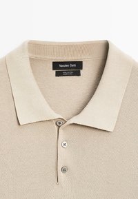 Beige katoenen polohemd met een geribbelde kraag, drie knoopsluiting en een textuur gebreid patroon. Label zegt "Massimo Dutti."