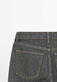 Donkerdenim jeans met een hoge taille, voorzien van dubbele achterzakken en contrasterend gele stiksels langs de naden. Soepele textuur.