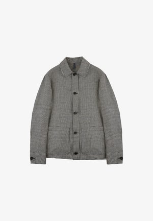 Chaqueta de cuadro vichy en blanco y negro, con cuello, cierre frontal de botones y dos bolsillos laterales. La tela tiene un acabado texturizado.