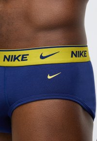 Μπλε ναυτικό ανδρικό boxer με κίτρινη ελαστική μέση που φέρει το "NIKE" και το λογότυπο Nike swoosh σε μπλε ναυτικό και κίτρινο. Λεία υφή.