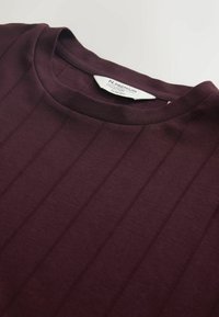 Burgundy t-shirt with a crew neckline, made of smooth fabric featuring vertical ribbed patterns and a slim fit design. Tag visible in the neckline.