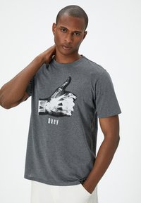 Camiseta gris con un estampado gráfico de una mano esquelética haciendo un gesto de pulgar hacia arriba con la palabra "Ok" debajo. Diseño clásico de cuello redondo.
