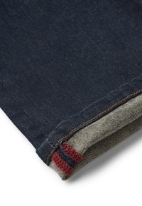 Ciemnoniebieska tkanina dżinsowa złożona, aby pokazać wewnętrzny szew z szarymi i czerwonymi detalami przeszycia na białym tle.