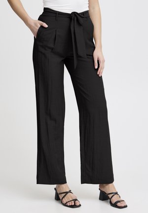 Black wide-leg trousers with a textured finish, featuring a tied waistband, front pockets, and a loose fit, paired with black block-heeled sandals.