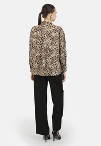 Blusa con stampa animale in tessuto leggero, con colletto e maniche lunghe. Abbinata a pantaloni neri e tacchi. Vista posteriore mostrata.