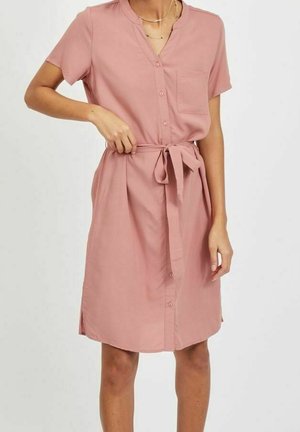 Abito a maniche corte rosa cipria con chiusura a bottoni frontale, tasca sul petto, cintura in vita e spacchi laterali. Tessuto morbido con una vestibilità rilassata.