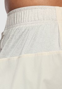 Lätta, krämfärgade atletiska shorts med en texturerad elastisk midja och en kontrasterande mjuk tygpanel vid fållen.