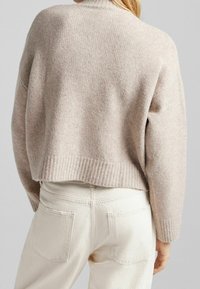 Beige gebreide trui met een geribde zoom en manchetten, met een losse pasvorm en een subtiele textuur, gecombineerd met lichtgekleurde denim jeans.