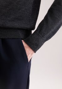 Dunkelgrauer Pullover mit geripptem Halsausschnitt und Bündchen, kombiniert mit marineblauen Hosen mit einer Seitentasche. Glatte Textur, taillierte Passform.
