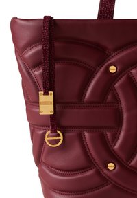 Tote in pelle bordeaux con motivi circolari a trapunto, hardware dorato e dettaglio a tracolla testurizzato. Presenta una placca con logo e un anello attaccato.