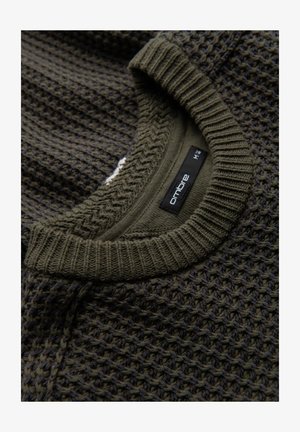 Tmavě olivově zelený pletený svetr s texturovaným vaflovým vzorem a žebrovaným límcem. Štítek uvádí "ombre", velikost M.