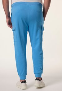 Blaue Baumwoll-Jogginghosen mit elastischem Bund, abgestuften Knöcheln und zwei Seitentaschen. Mit einer Gesäßtasche auf der rechten Seite.