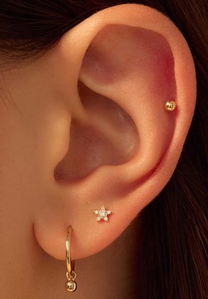 Gouden hoopoorbel met een hangende baldetails en een kleine stervormige stud met een heldere edelsteen, tegen een gladde huid achtergrond.
