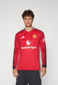Piros, hosszú ujjú focimez fekete részletekkel, az Adidas logójával, a Manchester United címerével, és fehér betűkkel a "Snapdragon" felirattal az elején.