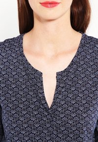 Námořnická halenka s květinovým potiskem, výstřihem do V a lehkou strukturou materiálu. Má opakující se vzor v kontrastních barvách.