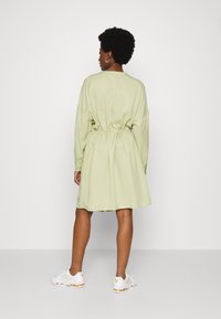 Vestido verde claro com mangas longas, cintura ajustada e uma saia fluida. Usado com tênis brancos. Textura simples e suave.