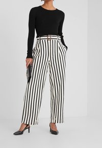 Haut noir à manches longues côtelées associé à un pantalon taille haute à jambes larges avec des rayures verticales noires et blanches. Chaussures à talons noires et pochette incluses.