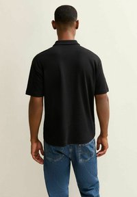 Zwart polo shirt met korte mouwen, gladde textuur en een klassieke kraag, in combinatie met blauwe denim jeans met achterzakken.