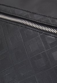 Black textured fabric with a geometric pattern, featuring a silver zipper and reinforced stitching. Smooth to touch, with a subtle sheen.
