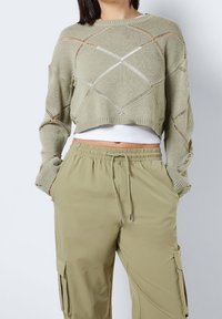 Ljust grön kortärmad tröja med öppet stickat diamantomönster och långa ärmar, kombinerad med beige cargobyxor med elastisk midja.